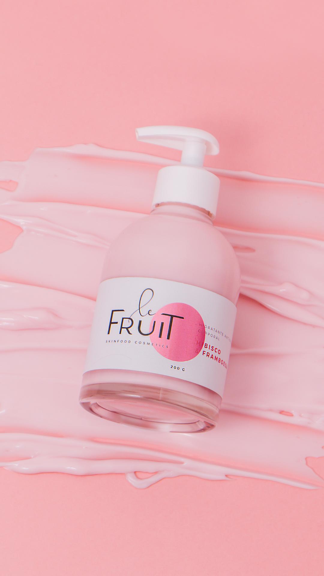 A foto mostra uma embalagem do hidratante da marca Le Fruit é constituída por um frasco de vidro com o rótulo da embalagem, enquanto o líquido hidratante está espalhado debaixo da embalagem.
