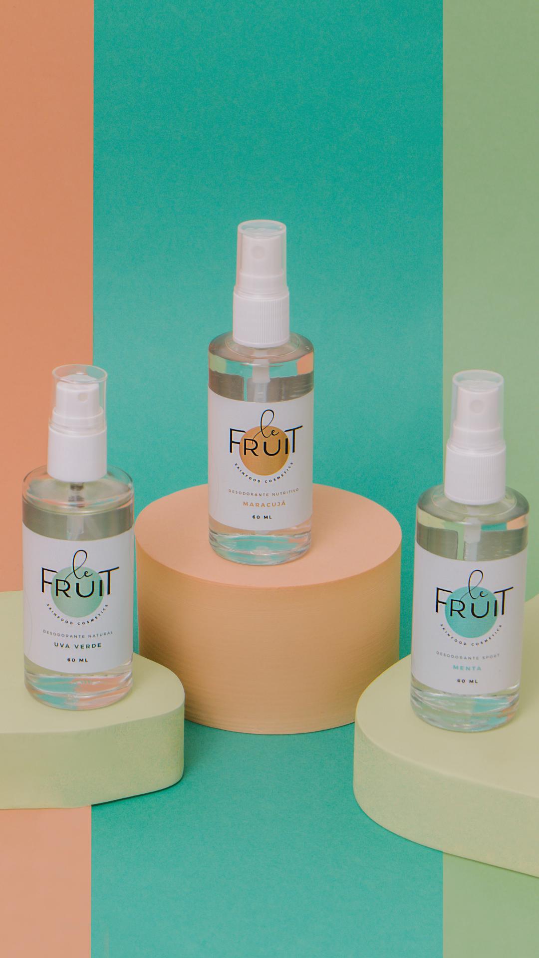 Imagem com os três desodorantes principais da Le Fruit na frente de um fundo colorido. Mostra os três frascos de vidro dos desodorantes de Maracujá, Uva Verde e Menta.