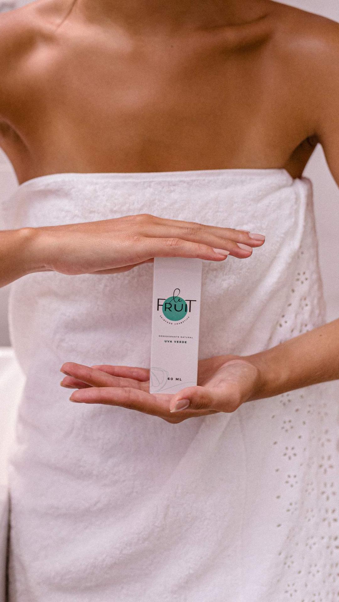 Uma mulher segurando uma embalagem de desodorante Sport Menta, com o corpo envolto em uma toalha, é retratada em um ângulo que não permite ver o rosto.